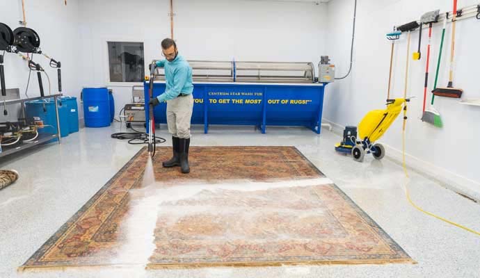 A professional using a pressure spray to deep clean a large oriental area rug