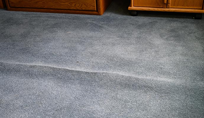 Buckled and wrinkled grey carpet requiring professional stretching