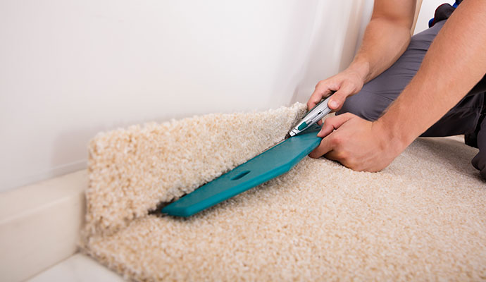 Person using a carpet stretching tool to adjust a beige carpet