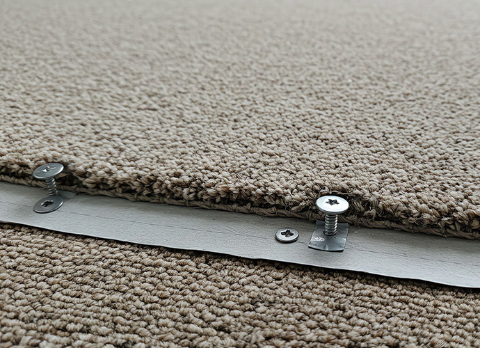 Close-up of metal screws being installed into a silver carpet transition strip