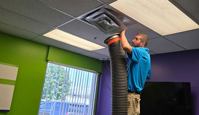 Technician cleaning ceiling air duct vent with vacuum hose