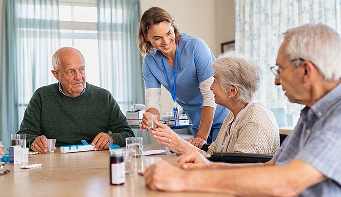 Caregiver assisting senior residents seated around a table in an assisted living facility