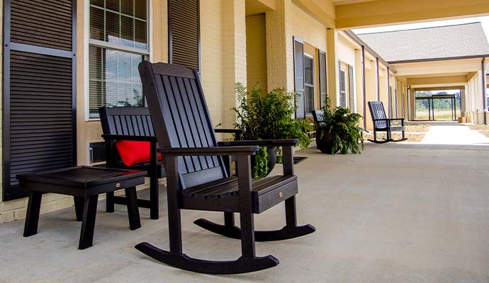 Covered porch of an assisted living facility furnished with rocking chairs and potted plants
