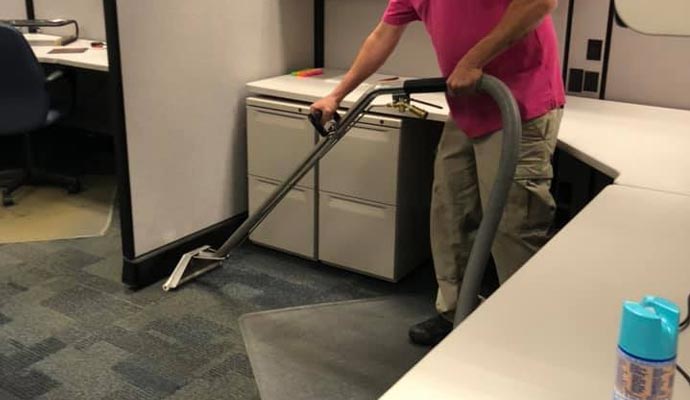 A professional cleaning the carpet in an office cubicle.