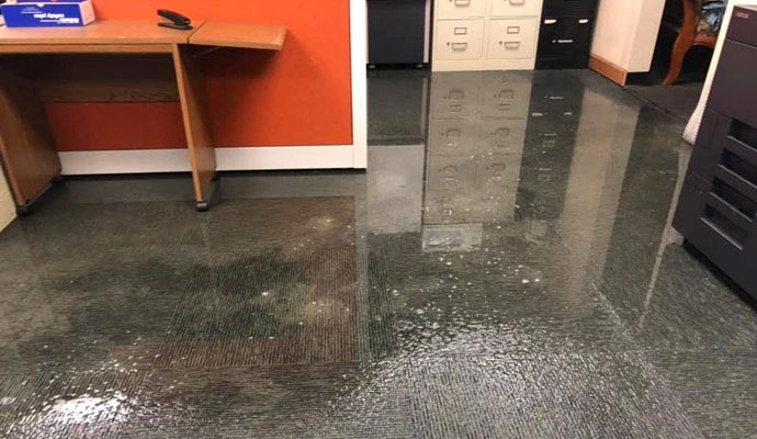 Commercial office space with standing water and visible indoor water damage across flooring surfaces