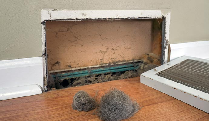 A very dirty air duct vent with clumps of dust removed.