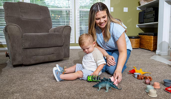 A mother and toddler playing with toys on a freshly cleaned, plush brown carpet in a home living room
