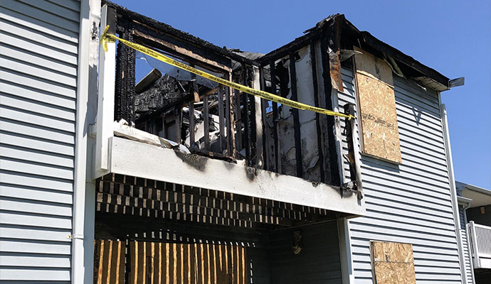 Burned apartment balcony with caution tape and boarded-up windows