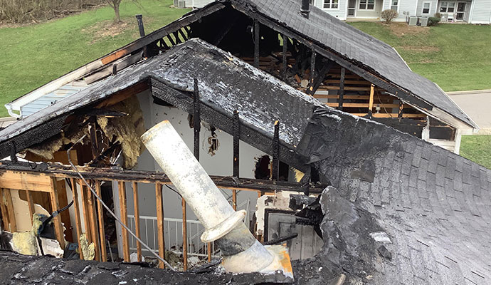 House with a burned, collapsed roof and exposed framing after a fire