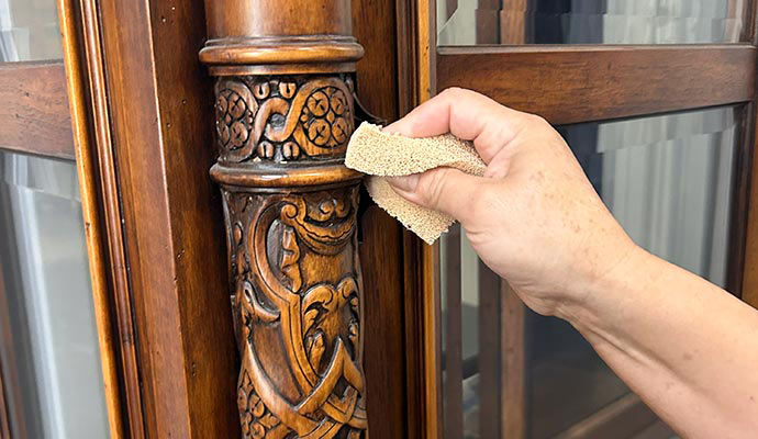 Hand cleaning and restoring detailed wooden furniture surface during professional contents restoration service