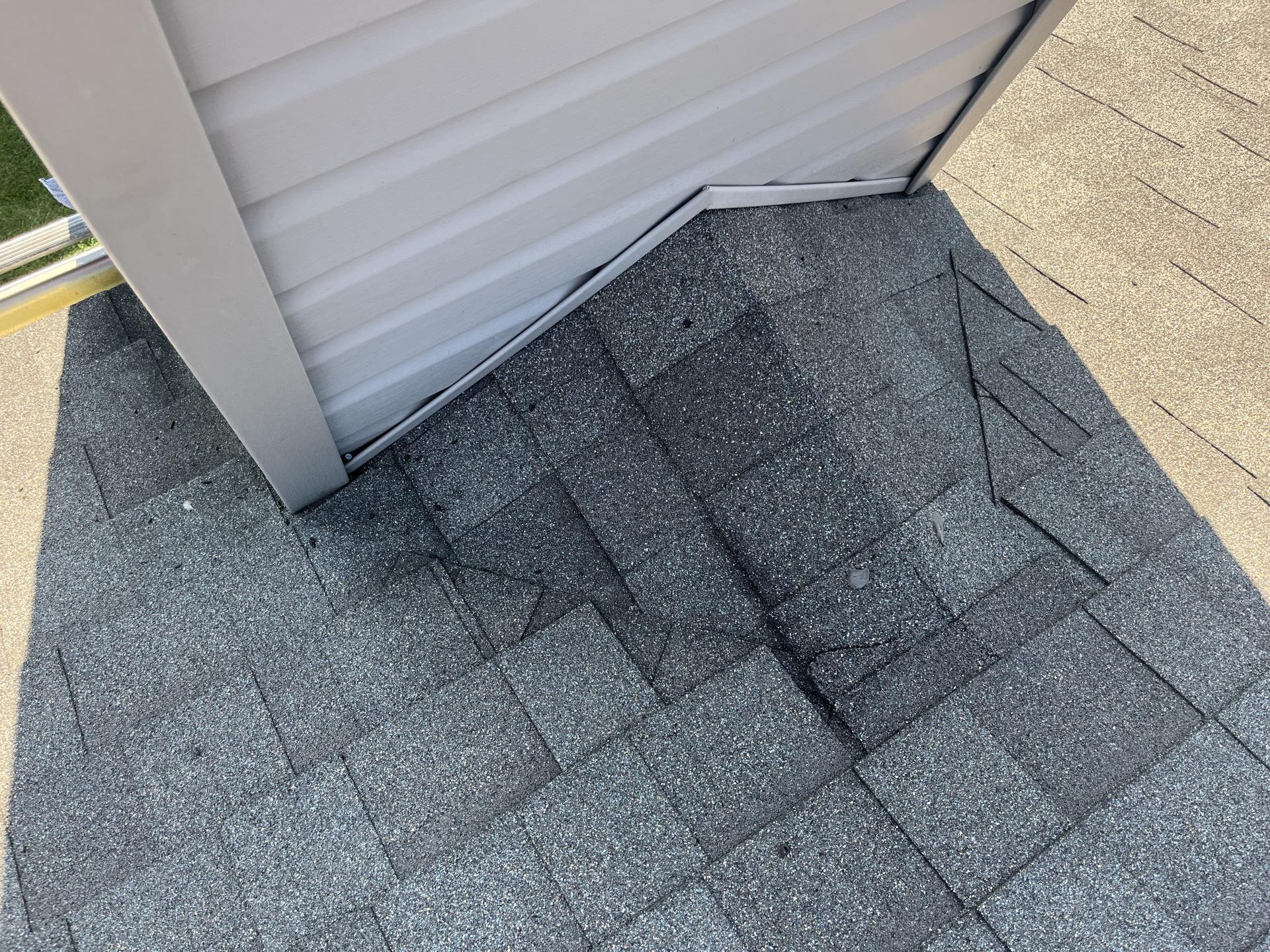 Overhead view of an asphalt shingle roof cricket and flashing junction behind a vinyl-sided chimney chase