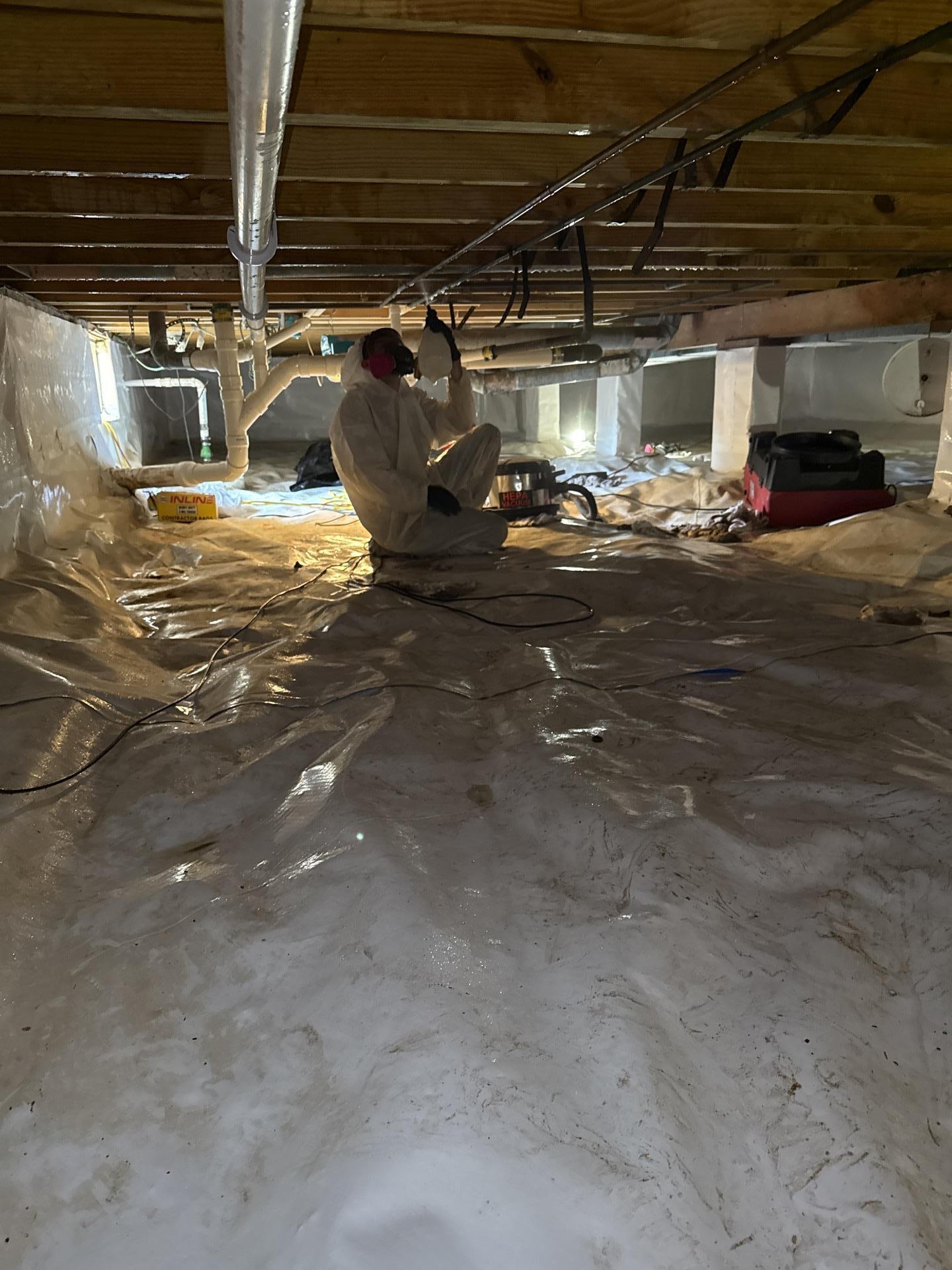 Professional technician in protective gear applying antimicrobial treatment to crawlspace joists during mould mitigation.