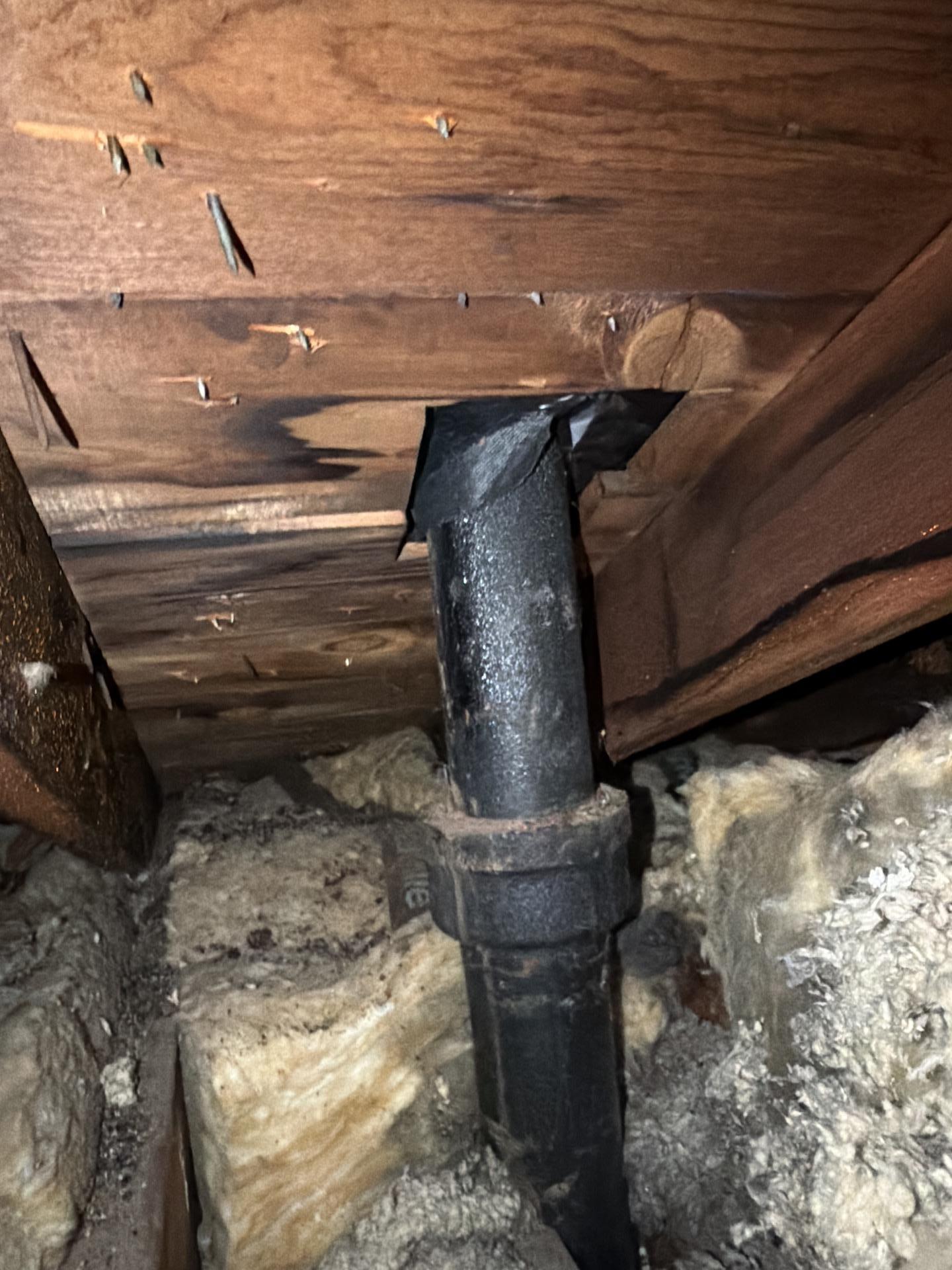 Underside of attic roof decking showing dark water staining and moisture ingress around a black vent pipe penetration.