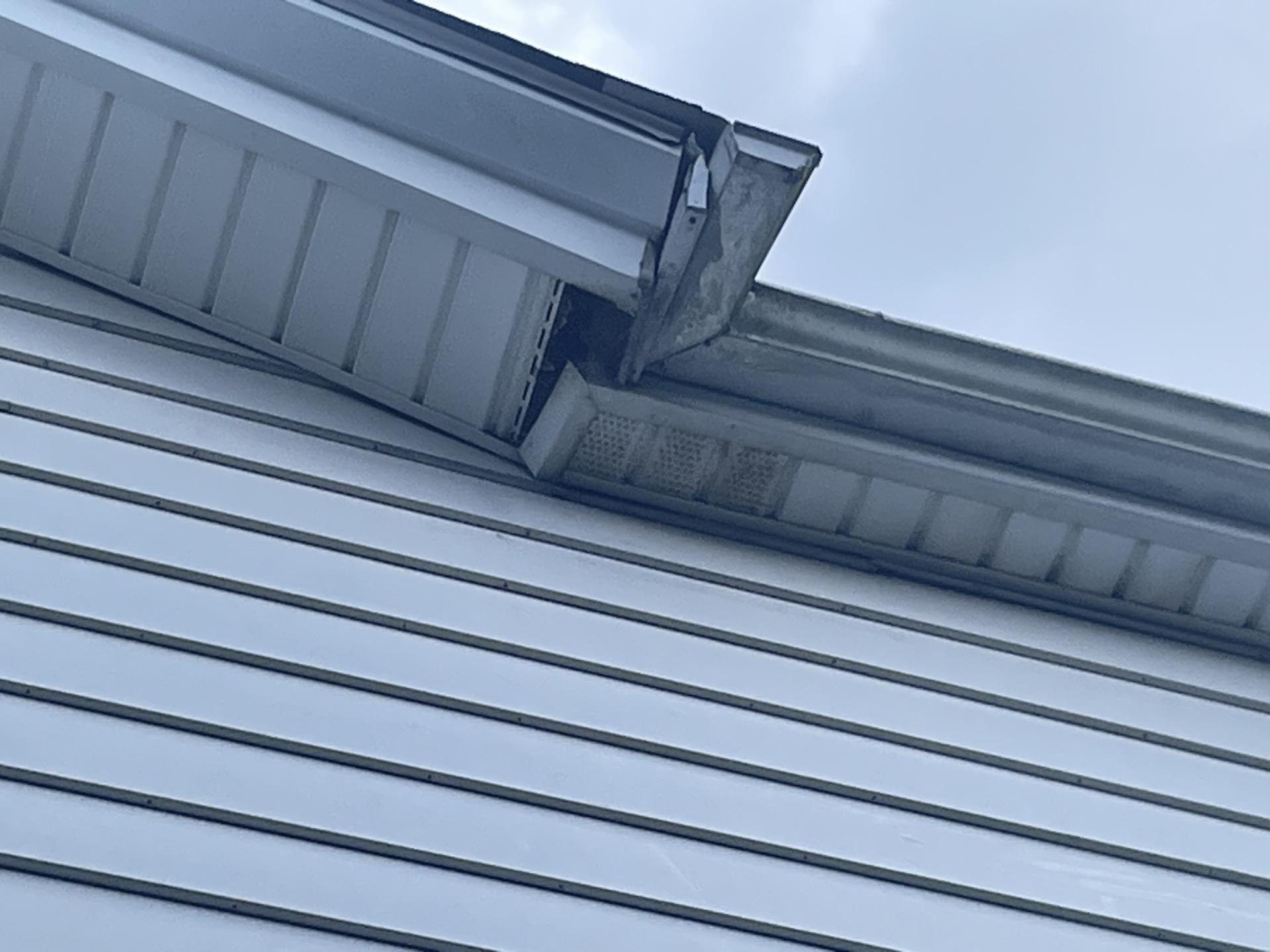 Close-up inspection of damaged guttering and detached soffit panels along an exterior roofline.