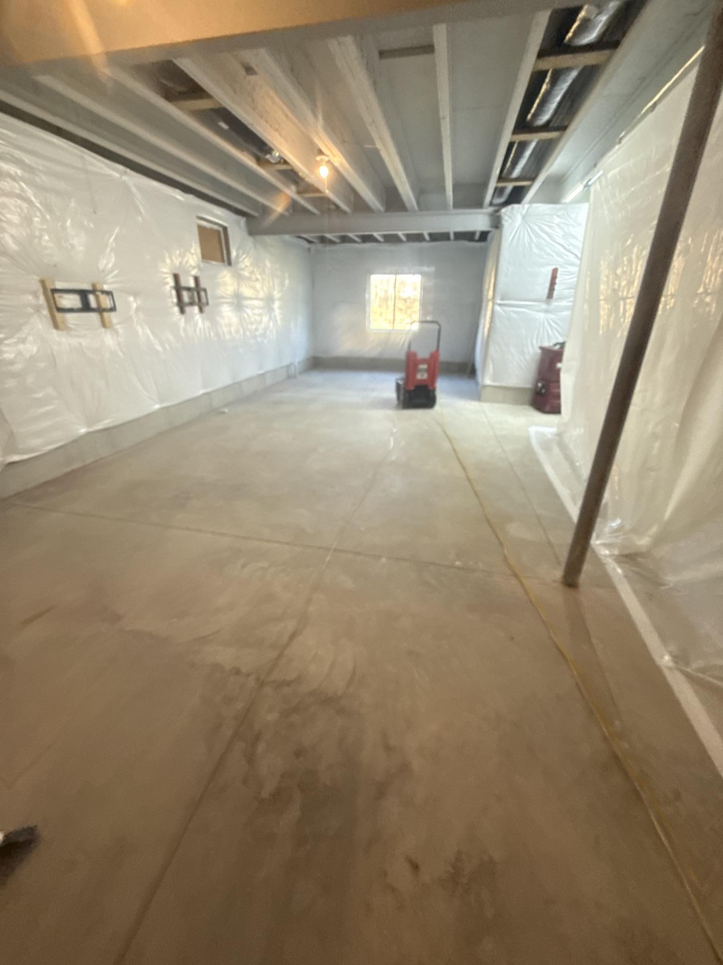Cleaned and contained basement with plastic sheeting on walls and drying equipment after mold remediation.