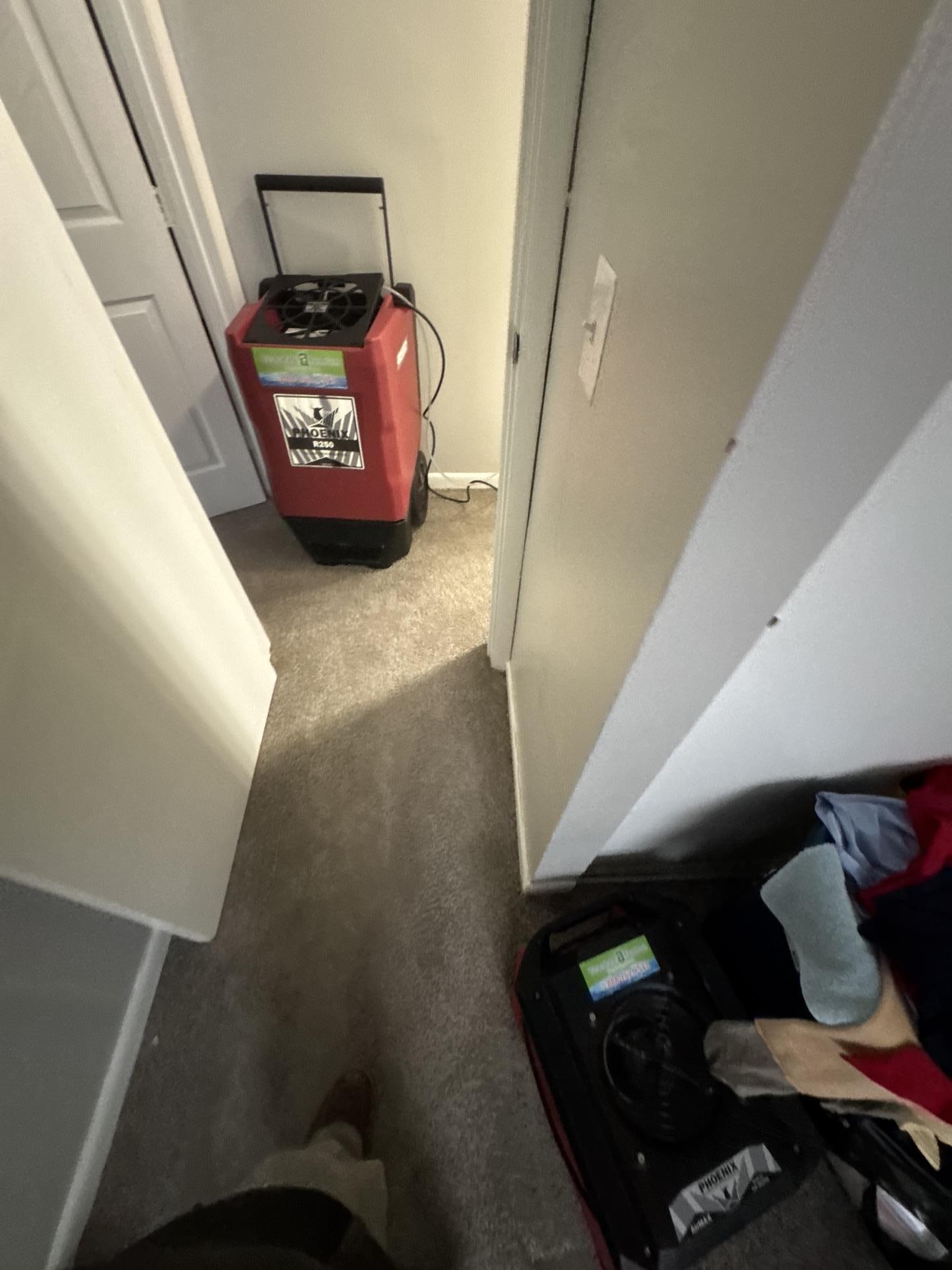 An industrial red dehumidifier and a black air mover positioned in a hallway to remove moisture from the air and carpet after water damage.
