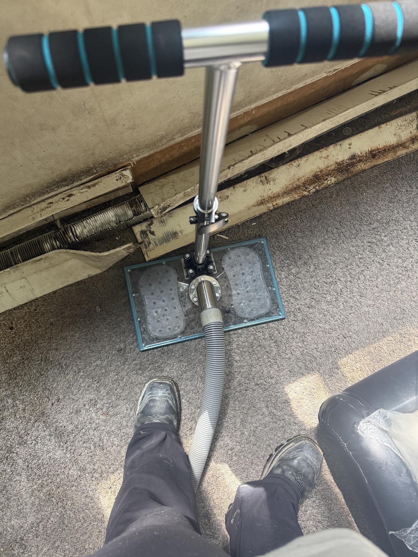 Technician operating a weighted water claw extraction tool connected to a vacuum hose on saturated carpet.