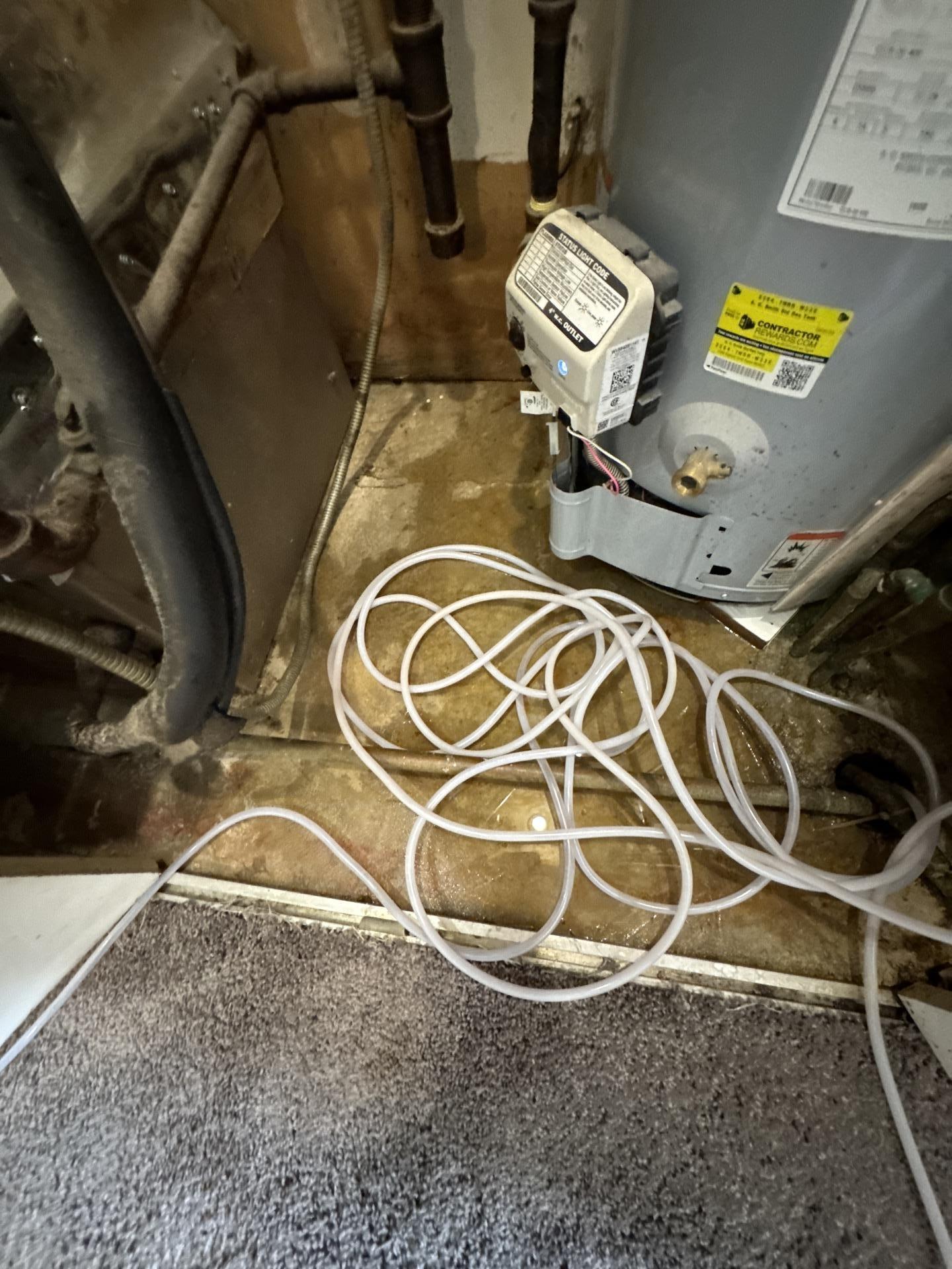 Close-up of standing water on the floor of an apartment utility closet, showing pipes and a water heater base.