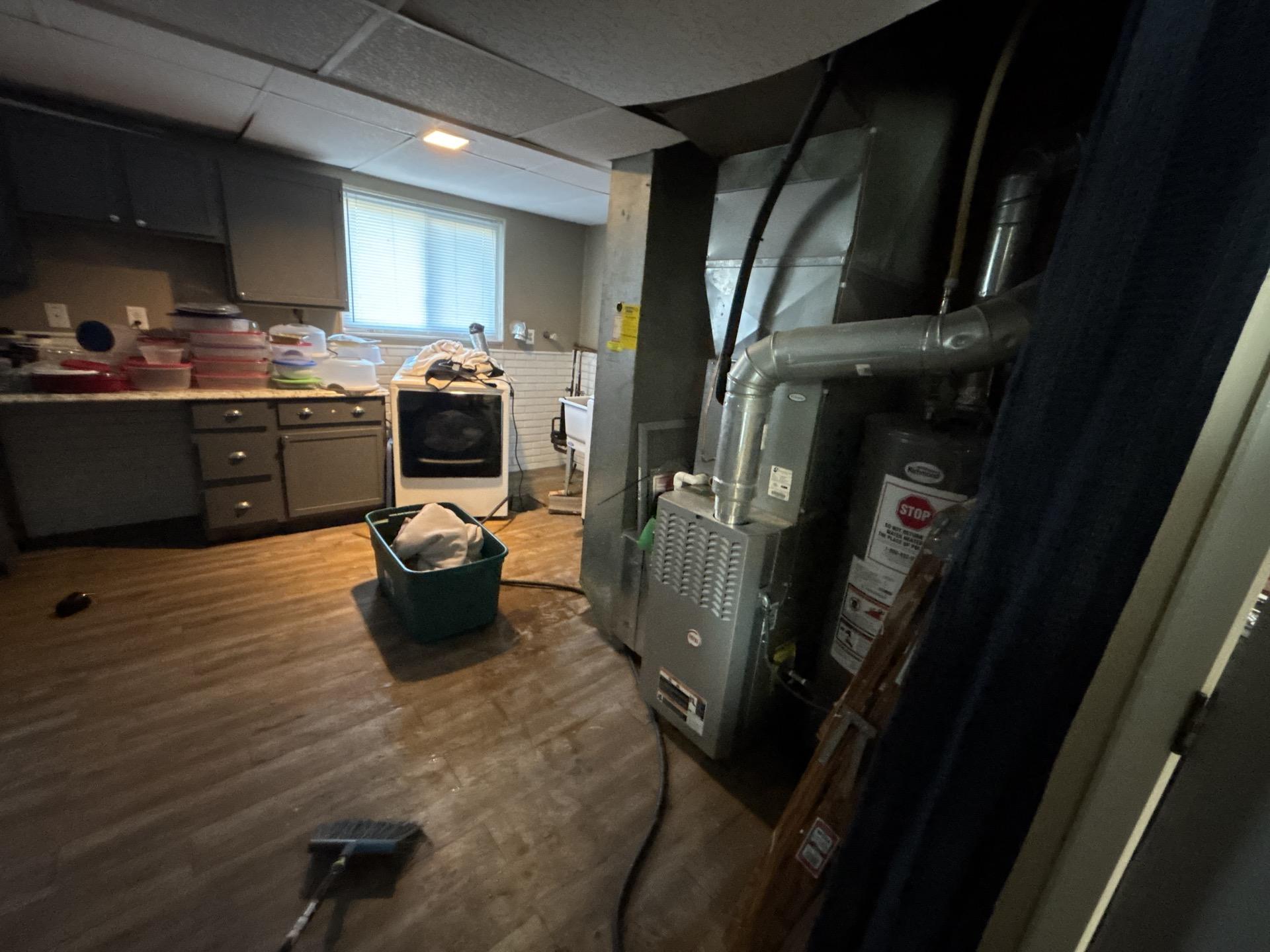 Basement utility and laundry room with HVAC unit, water heater, and washer, featuring visible water damage on the floor during cleanup.