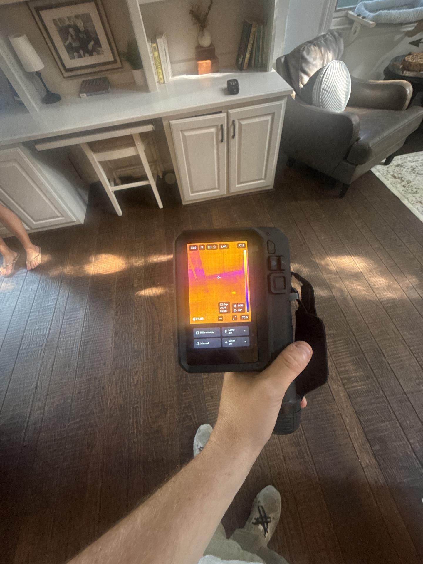 Technician using a FLIR thermal imaging camera to detect hidden moisture behind residential built-in cabinetry.