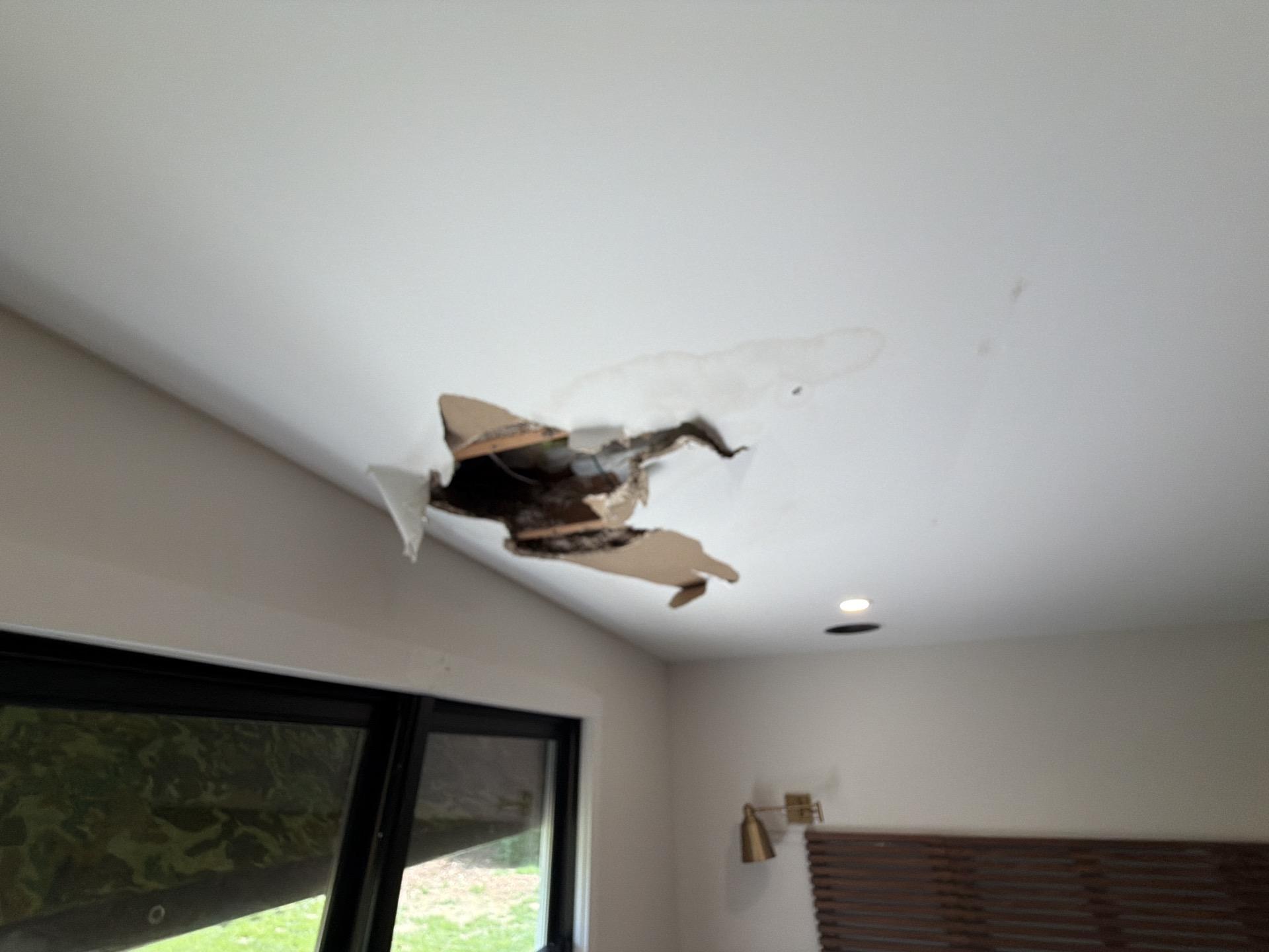A large, irregular hole in a residential ceiling showing severe water damage to drywall, indicating the extent of the water intrusion before restoration.