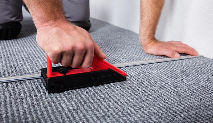 A close-up of a flooring professional using a red precision cutting tool