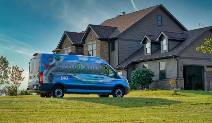 A branded service van parked on the green lawn in front of a large two-story suburban house