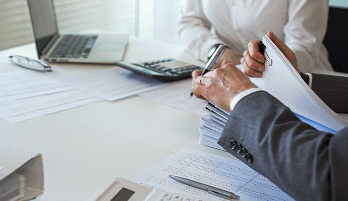 A professional reviewing a stack of documents beside a calculator and laptop