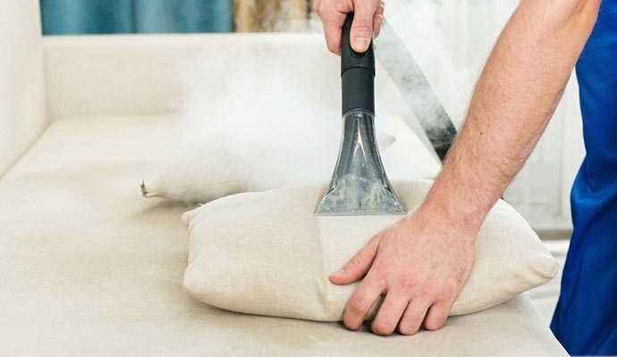 A professional cleaner using a steam extraction tool to deep clean a beige throw pillow