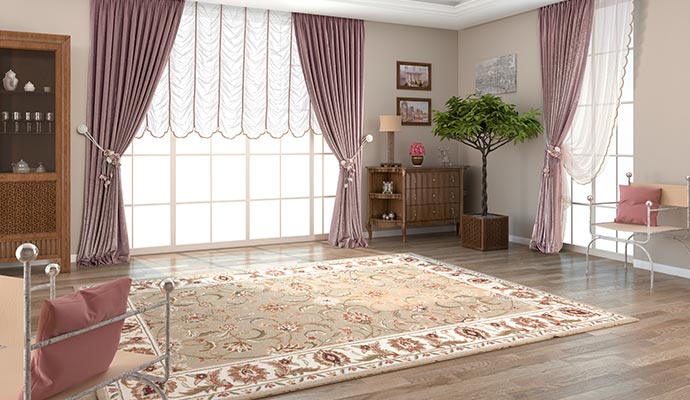 A bright, elegant living room with large windows, long purple drapes, and a large, patterned area rug placed on a hardwood floor