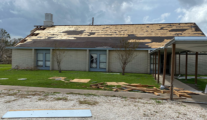 Commercial building with severe storm damaged roof missing shingles and exterior debris after weather event