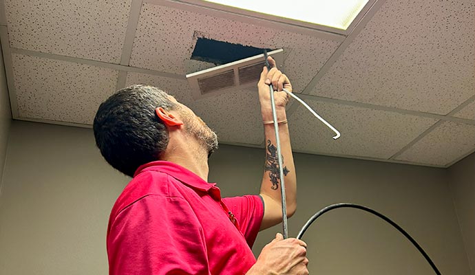 Technician cleaning ceiling air duct vent with rotary brush tool