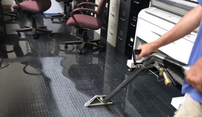 A technician is extracting water from carpet using portable water extraction machine