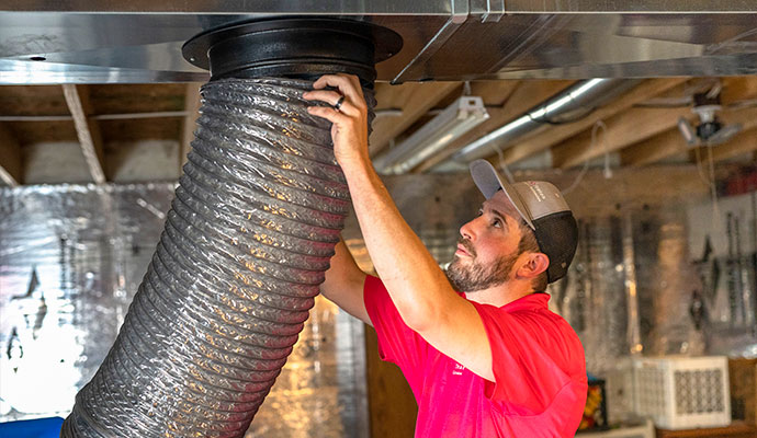A technician handling a flexible air duct connected to ceiling ductwork