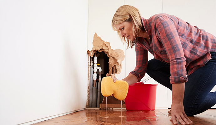 A person cleaning plumbing leak damage water from wooden floor using a sponge