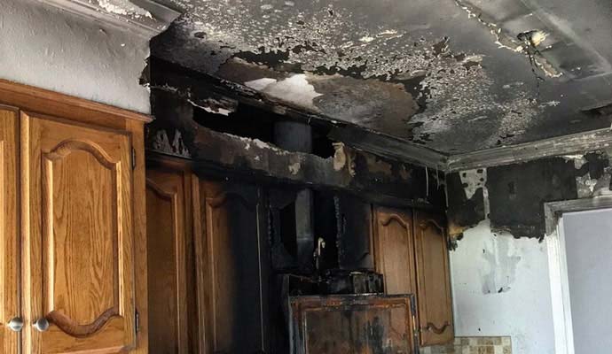 Charred ceiling and fire damaged wooden cabinets in a residential kitchen.