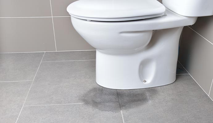 Water leaking from the base of a toilet onto a tile floor.