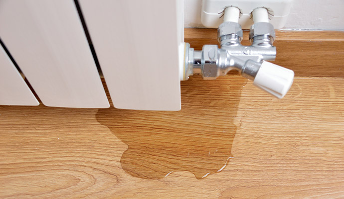 Wall-mounted radiator leaking water onto a light wood laminate floor