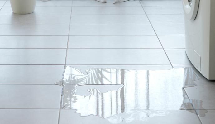 Water leaking from a washing machine onto a tile floor.